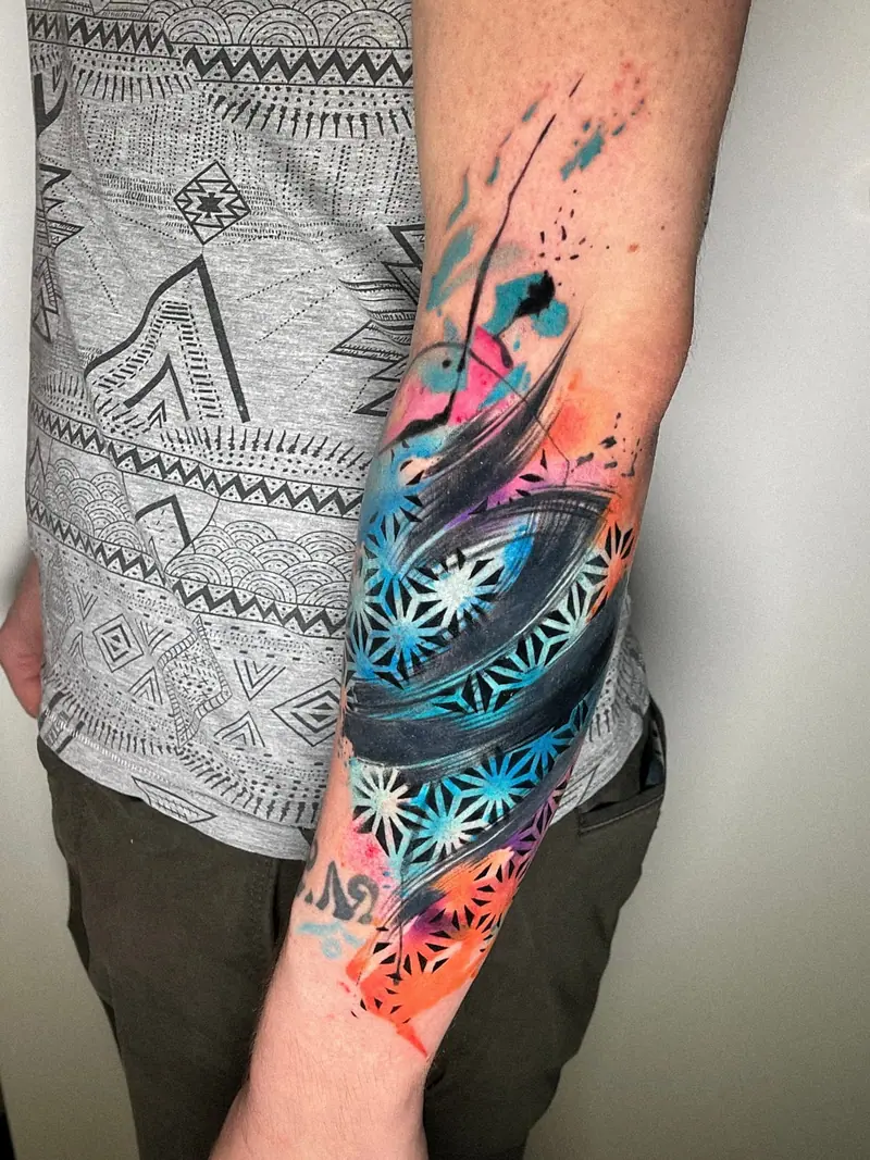 Abstraktes Unterarm-Tattoo mit geometrischen Formen und Farbspritzern, tätowiert von Maya.