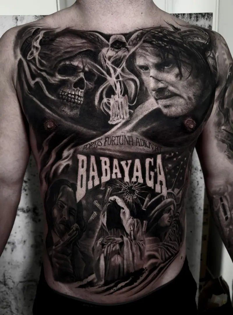 Brusttattoo im Black-&-Grey-Realismus mit Totenkopf und Filmmotiven, Schriftzug „Babayaga“, von Sabina.