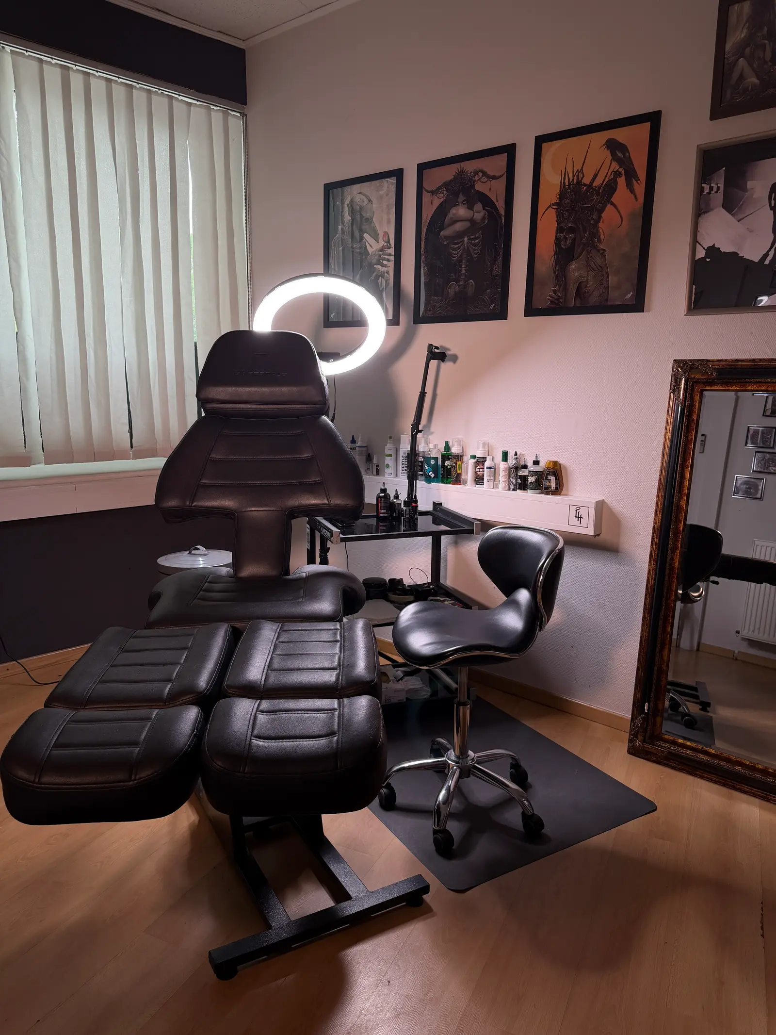 Ruhiger Behandlungsraum der Last Hope Tattoo Gallery bei Tageslicht, mit Tattoo-Liege, Farbregal und großem Spiegel.